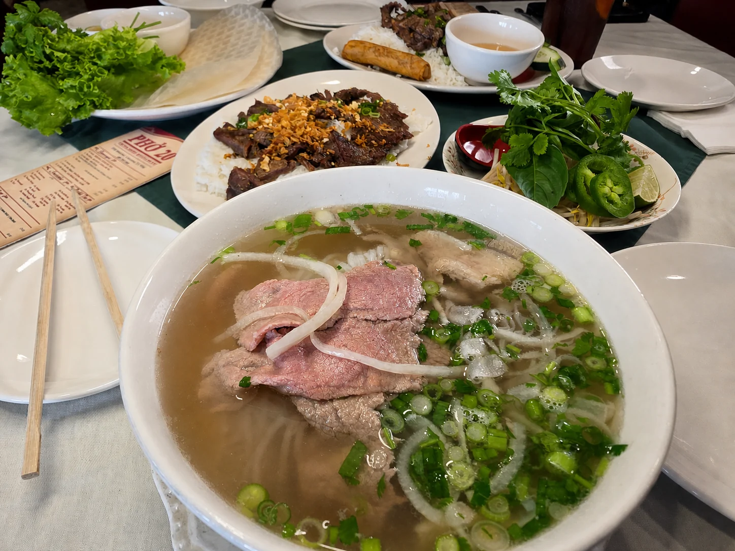 A bowl of house-special beef pho surrounded by dishes on a table at Phở 20 in Galveston