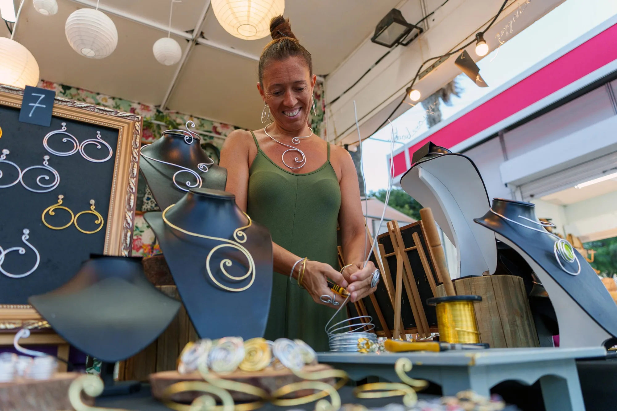 An artisan making wire jewelry at an outdoor market.