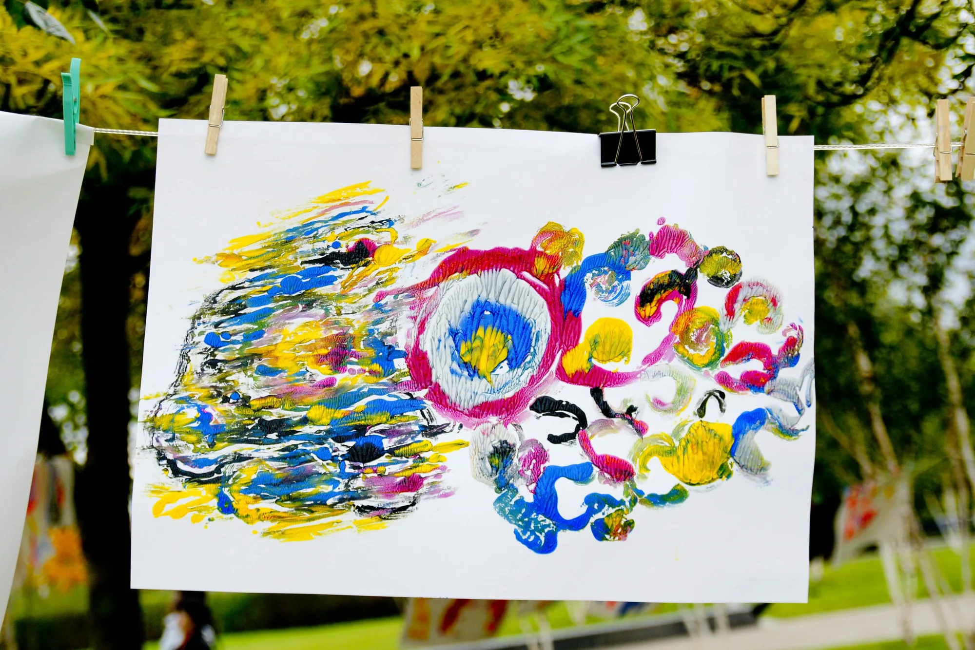 Colorful abstract finger paintings clipped to a line outdoors.